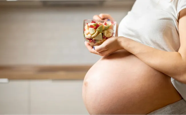 Pregnant woman holding glass of fresh fruit salad for healthy pregnancy nutrition